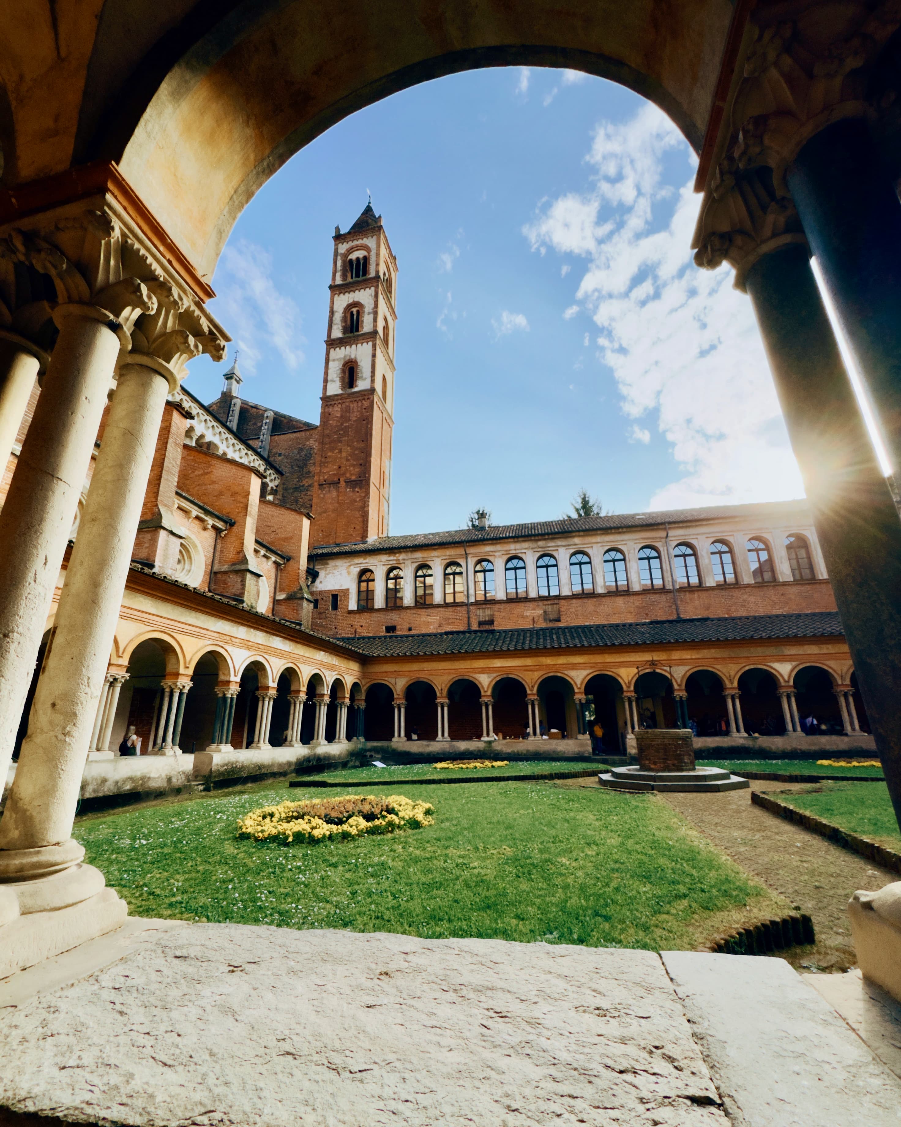 A big medieval-looking tower stands tall over the cloister of the basilica, seen through an ornate archway.