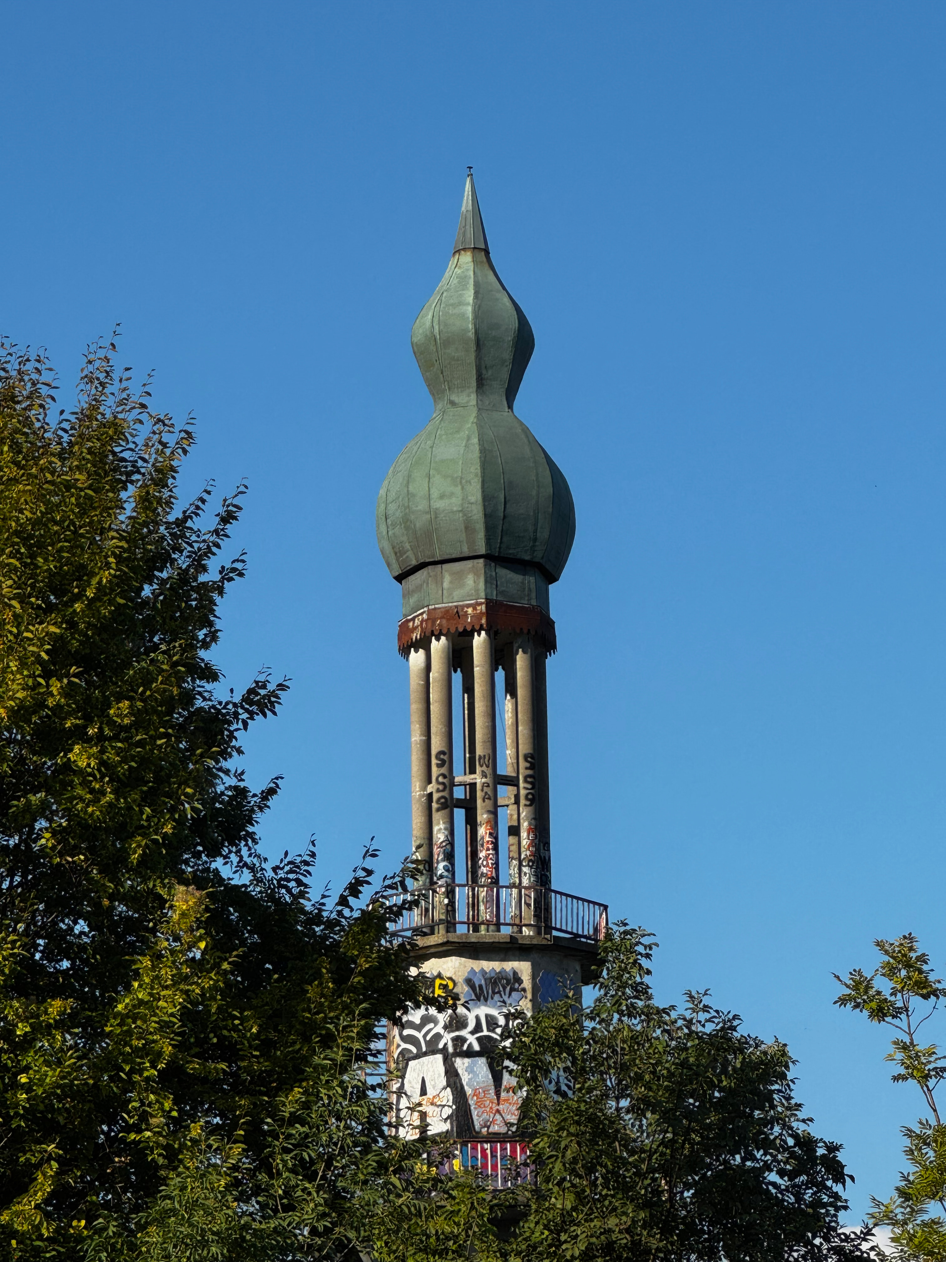 The graffiti-covered onion-domed minaret tower rising above trees at the abandoned ghost town of Consonno, Italy.