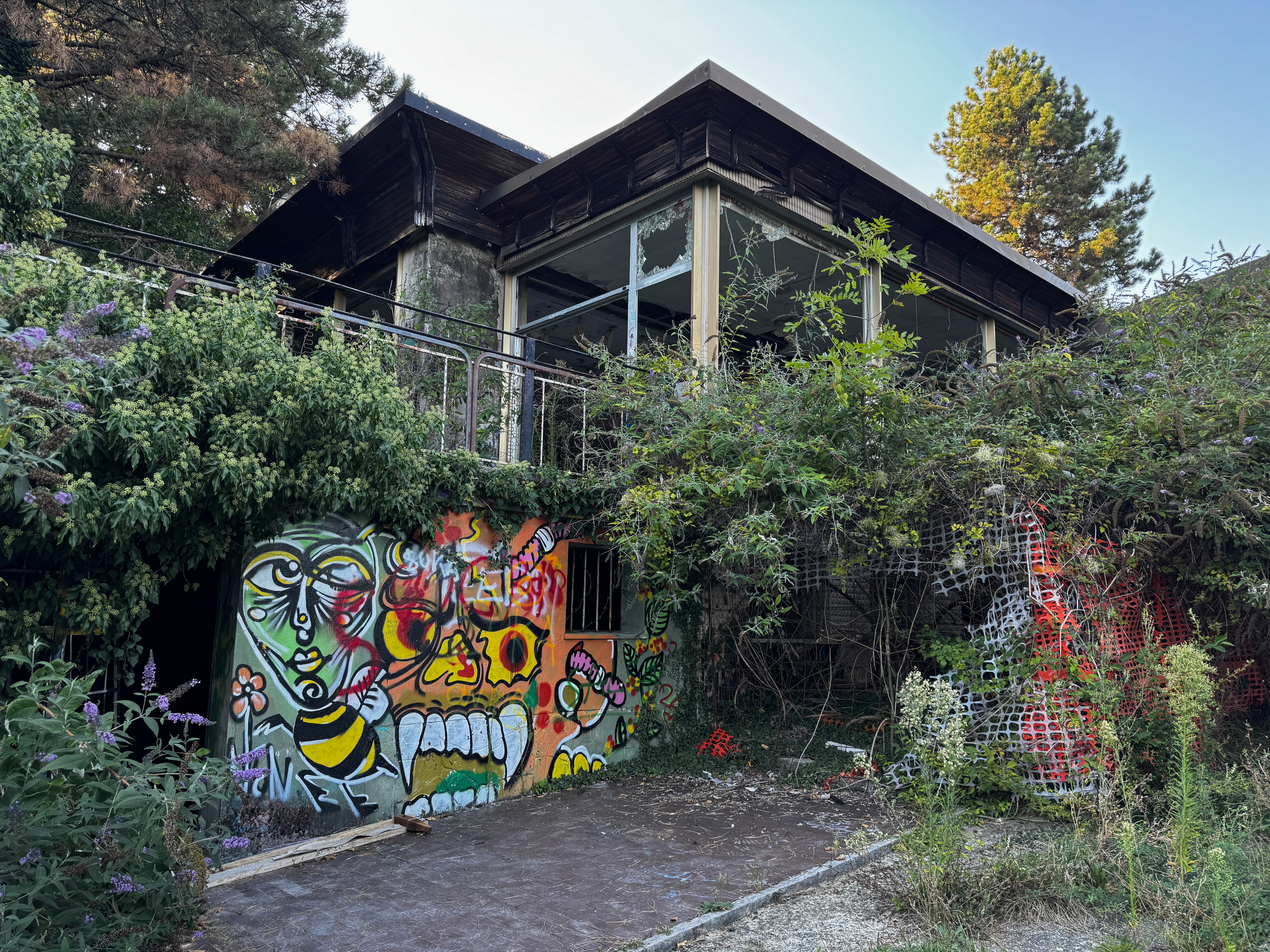 An abandoned, overgrown building at Consonno covered in colorful graffiti, with vegetation climbing over its balcony and broken windows.