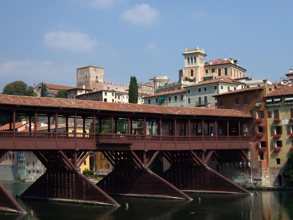 Picture of a brownish red wooden bridge, connected to stone buildings in one side of the river