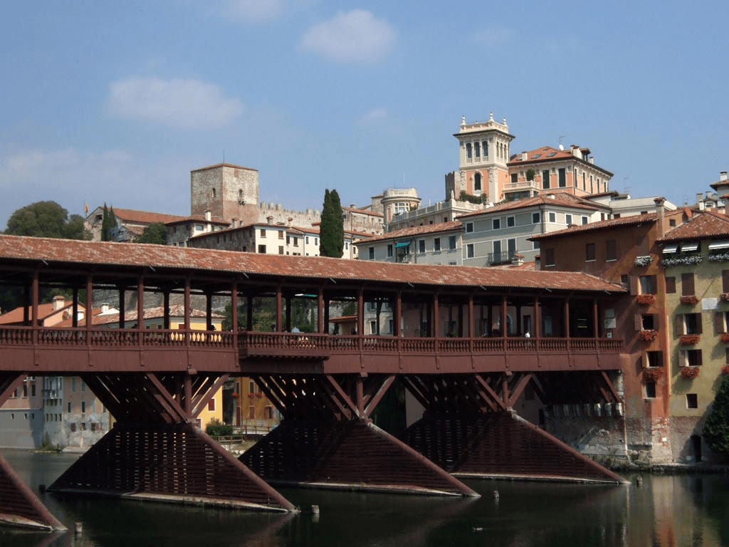 Picture of a brownish red wooden bridge, connected to stone buildings in one side of the river