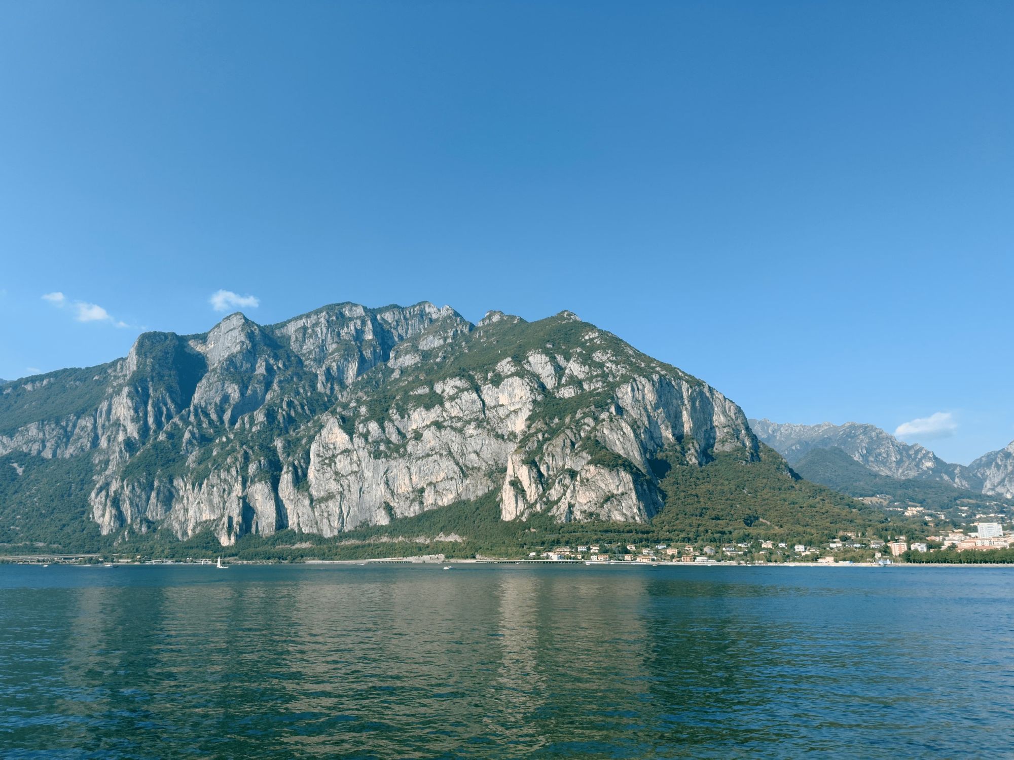 The rocky cliffs of Monte Coltignone rising above Lake Como, seen from Valmadrera, with sailboats on the water below.