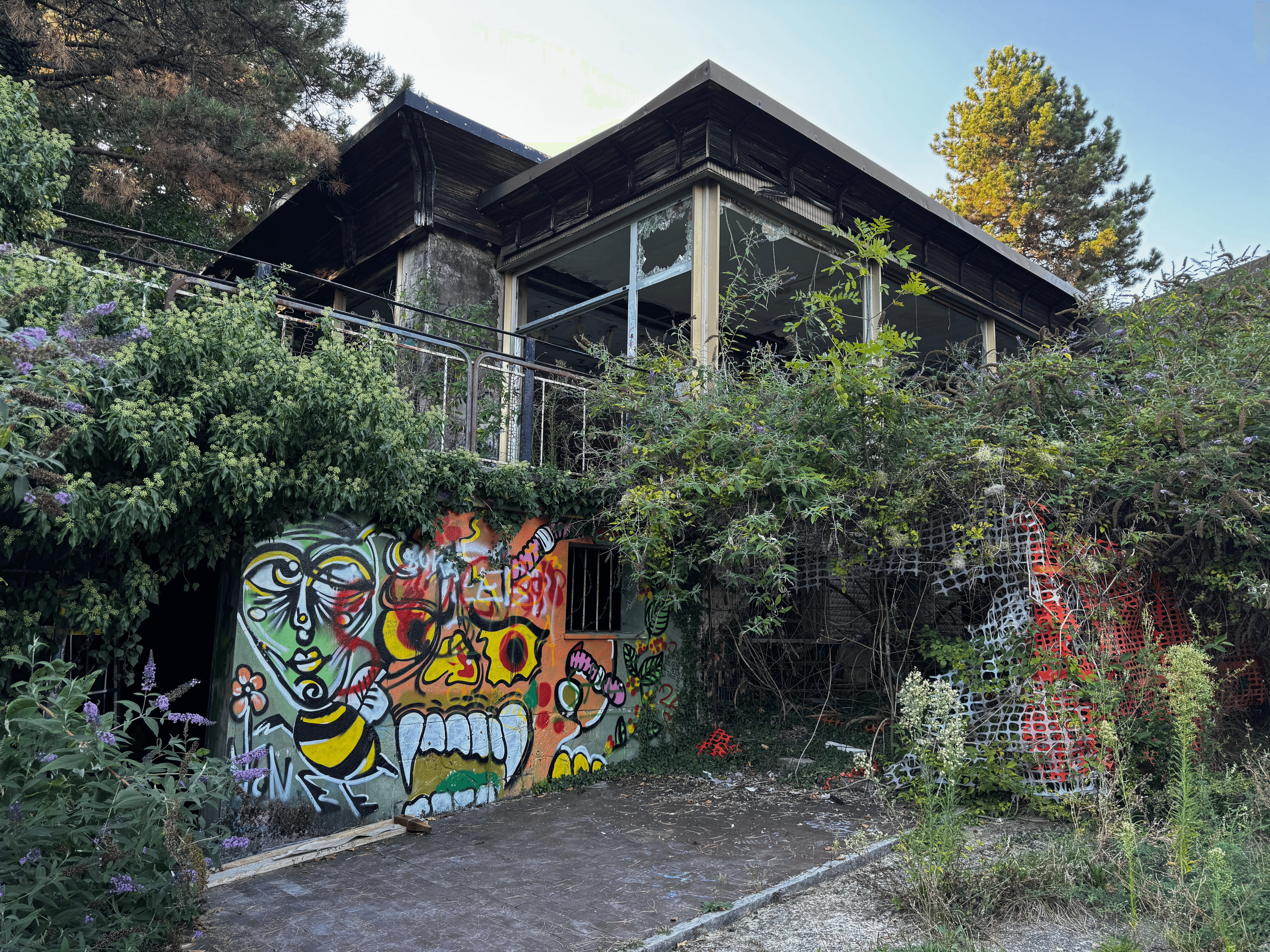 An abandoned, overgrown building at Consonno covered in colorful graffiti, with vegetation climbing over its balcony and broken windows.